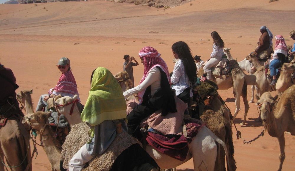 A group of students riding camels in the desert.